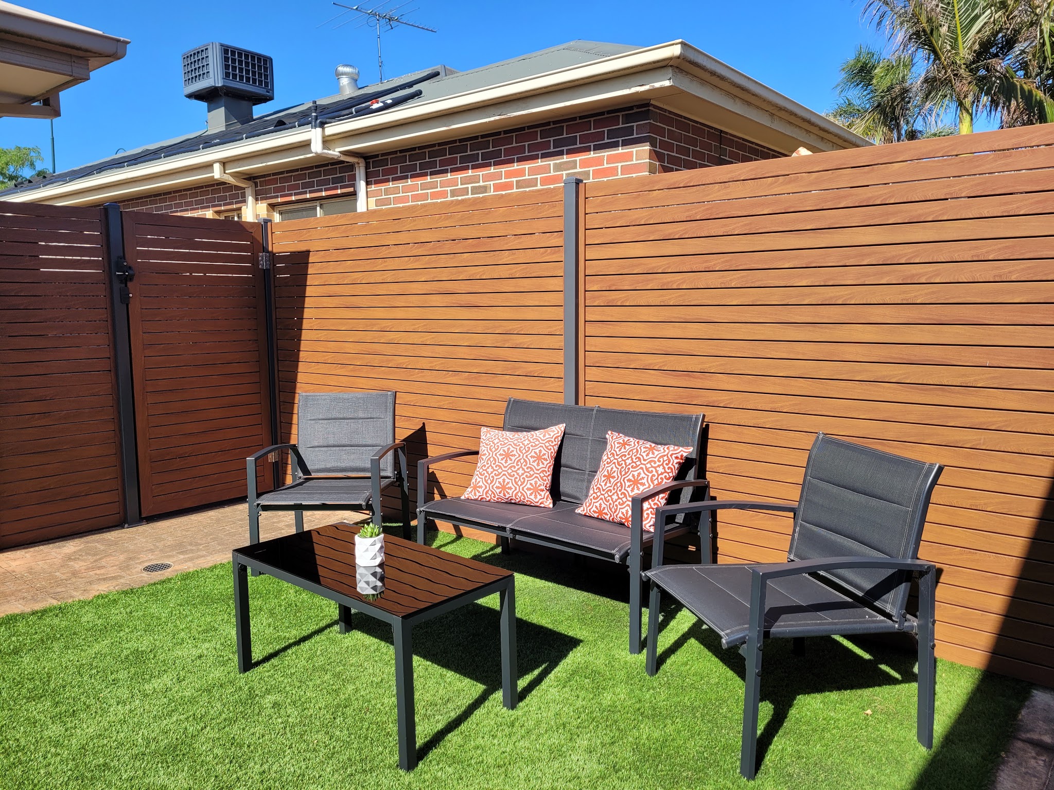 Woodgrain slat privacy fence with a matching lockable gate around a backyard seating area